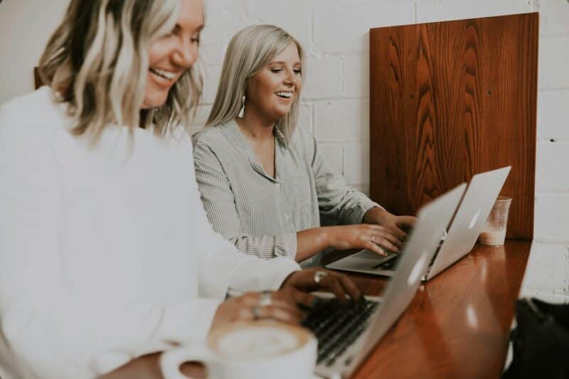 Two females sitting at a desk typing on latoptops.