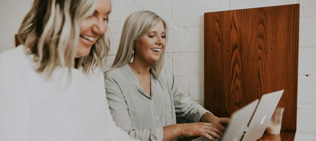 Two females sitting at a desk typing on latoptops.